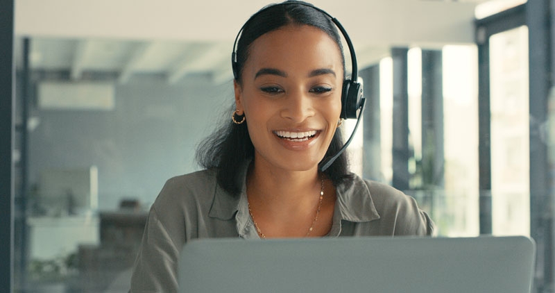 A customer service representative with a headset sits at a computer smiling